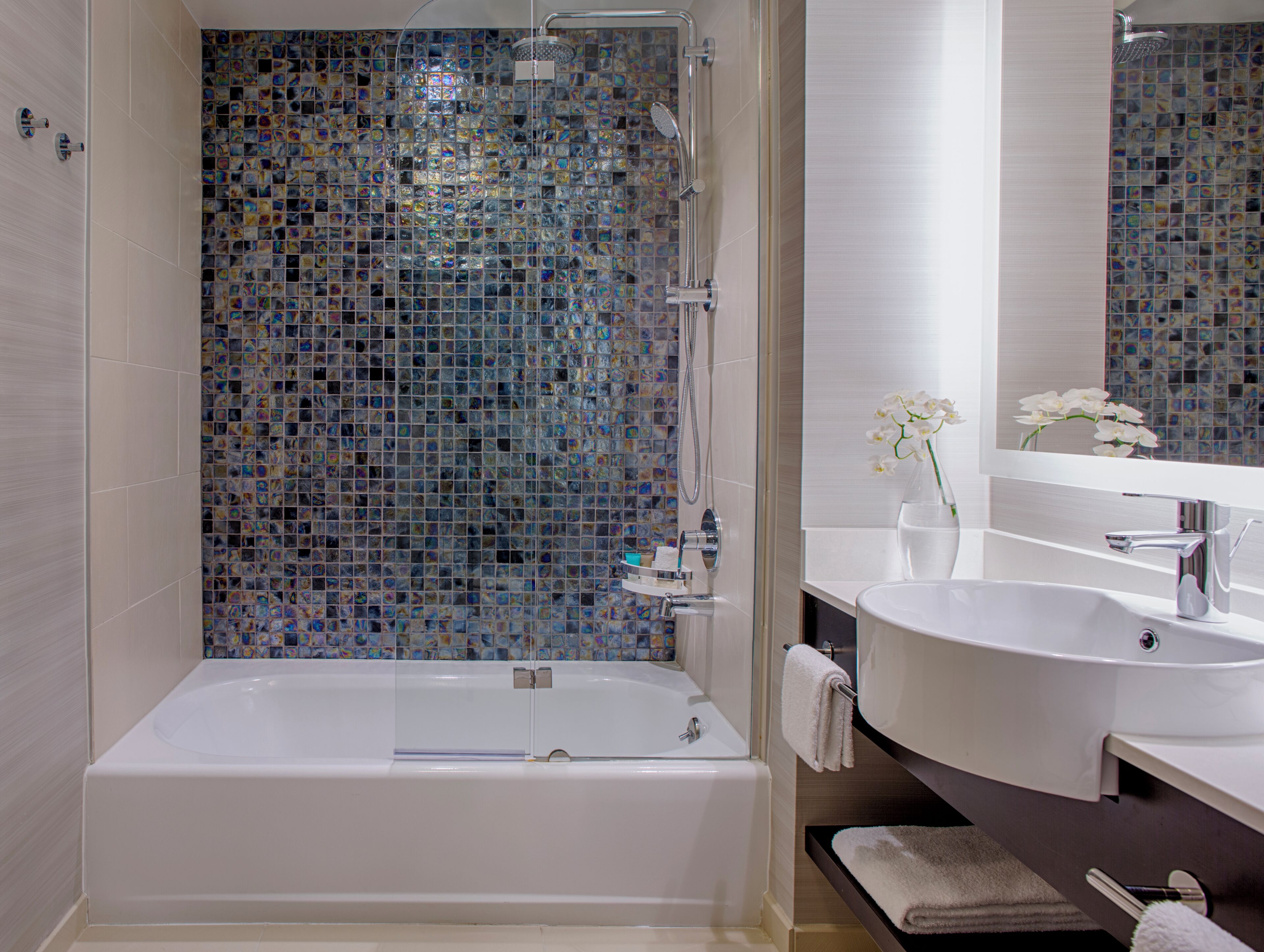 A modern bathroom with a glass-enclosed shower, a white bathtub, and a vanity with a mirror.