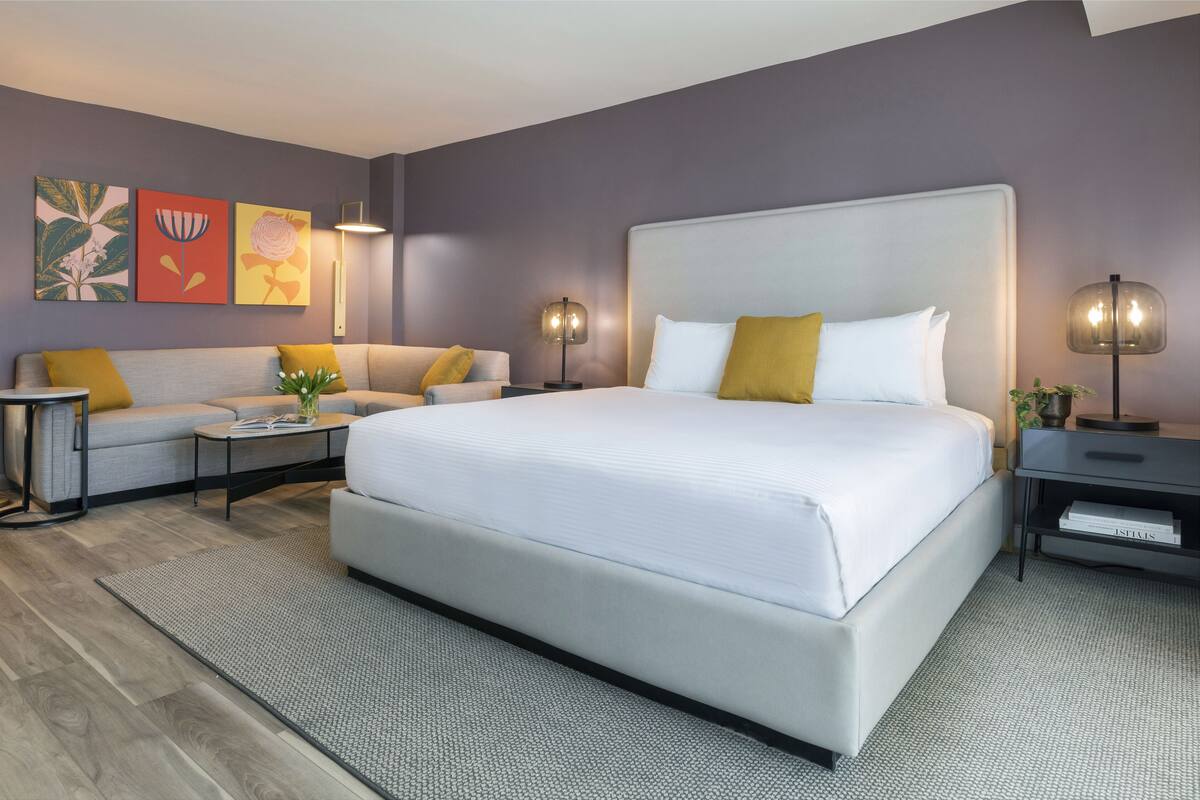 A modern hotel room with a large bed, a sofa, a coffee table, and a nightstand.