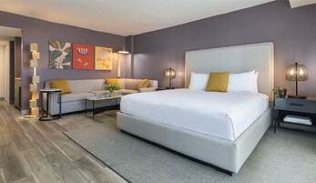 A modern hotel room with a large bed, a sofa, a coffee table, and a nightstand.