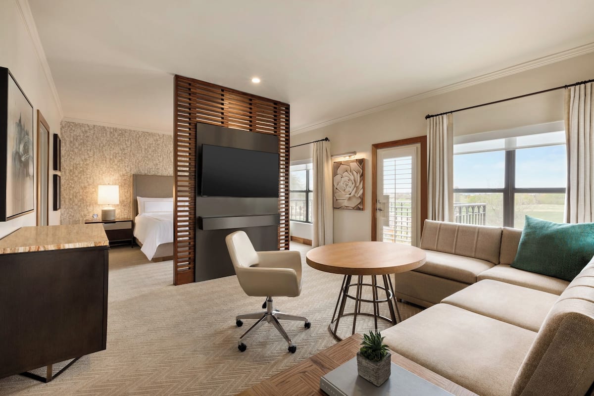 Ein Hotelzimmer mit Bett, Schreibtisch, Stuhl, Sofa, rundem Tisch und Fernseher.