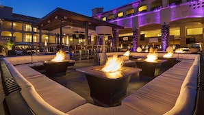 An outdoor seating area with fire pits and cushioned seating, overlooking a building with multiple balconies and a bar. - Fairmont Scottsdale Princess (Scottsdale)
