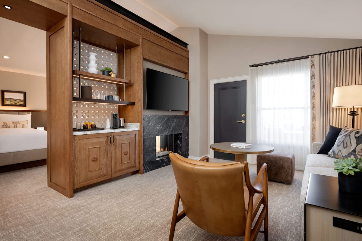 Ein modernes Hotelzimmer mit Holzschrank, Flachbildfernseher, Kamin, rundem Esstisch und einer Pflanze auf einer Couch.
