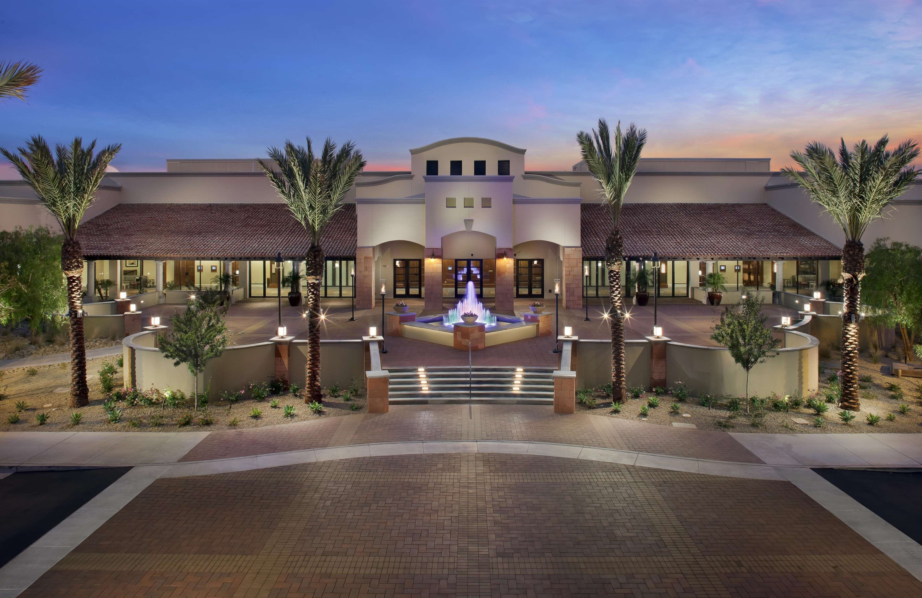 A hotel with a central fountain, palm trees, and a brick pathway leading to the entrance.