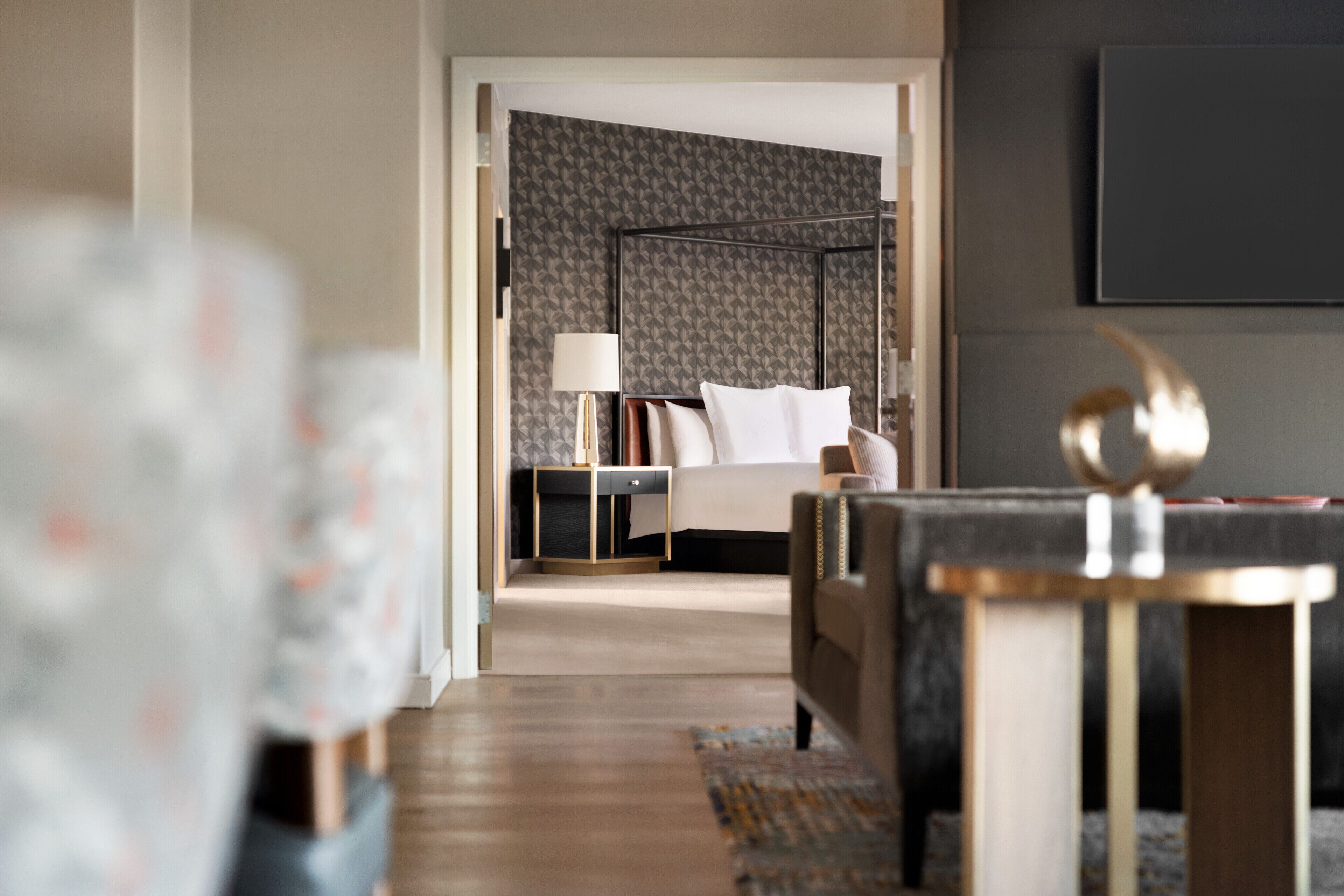 Une chambre d’hôtel moderne, équipée d’un lit, d’une table de chevet, d’une lampe et offrant une vue sur le couloir.