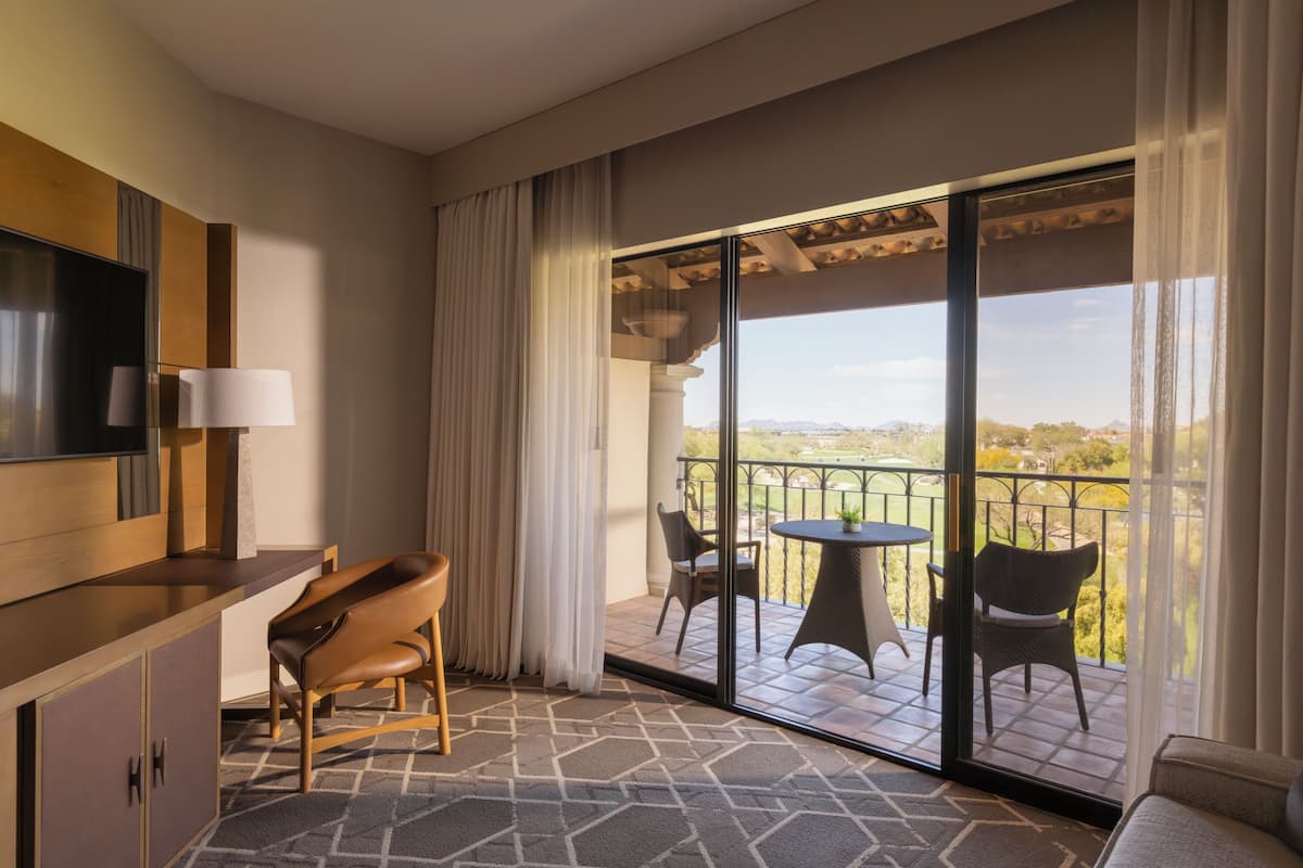 Ein Hotelzimmer mit Balkon, Fernseher, Sofa und Esstisch mit Stühlen.