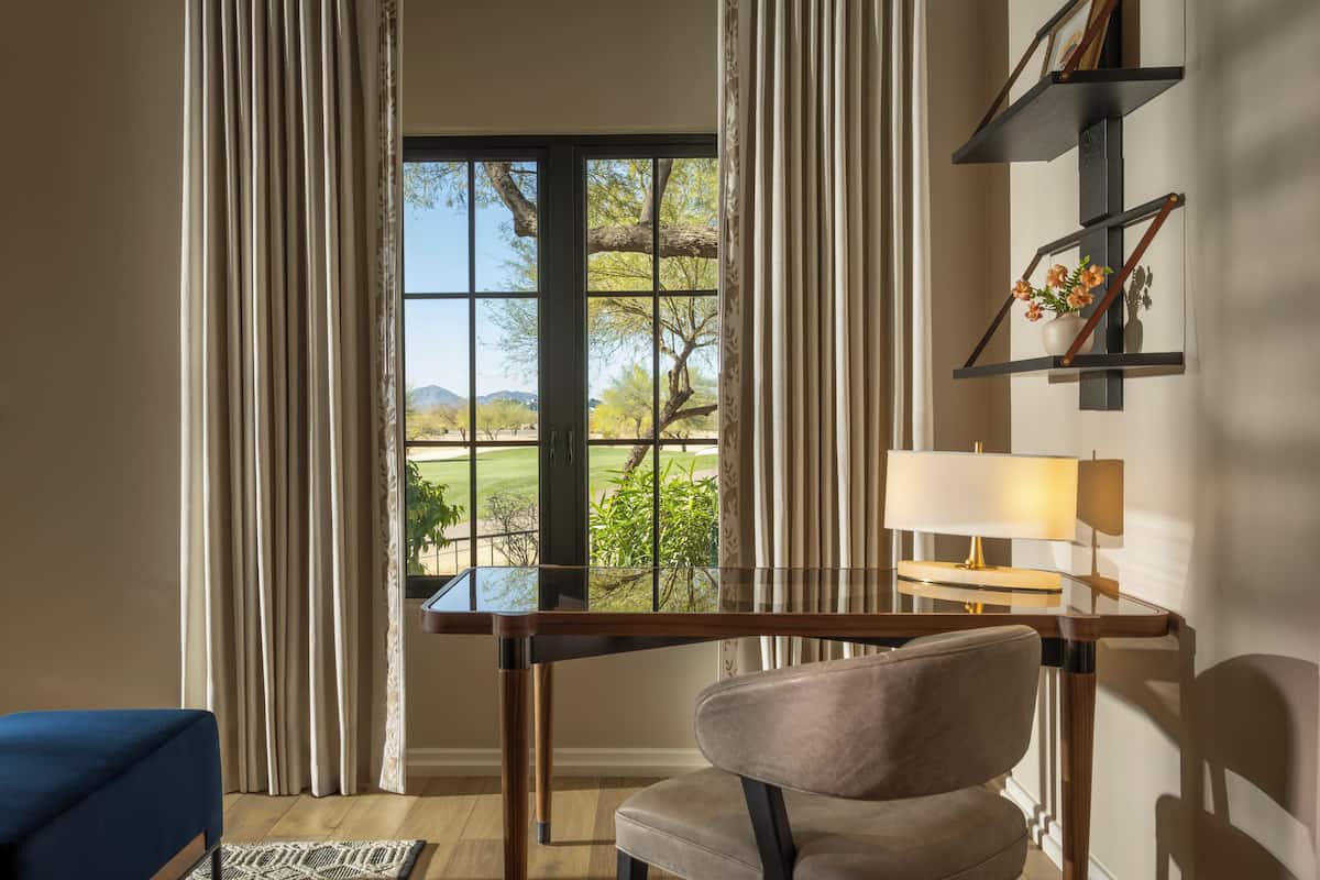 Ein Zimmer mit Schreibtisch, Stuhl und Blick auf einen Golfplatz durch ein großes Fenster.