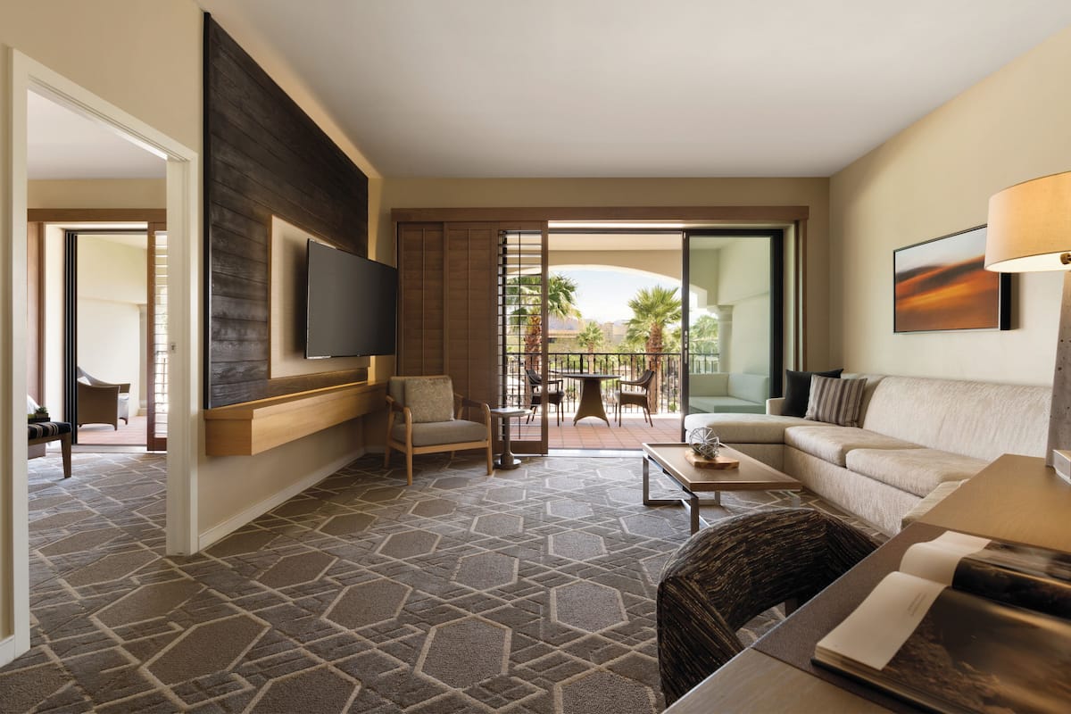 Ein Hotelzimmer mit großem Flachbildfernseher an der Wand, einer Couch, einem Couchtisch und einem Essbereich mit Stühlen und Tisch.