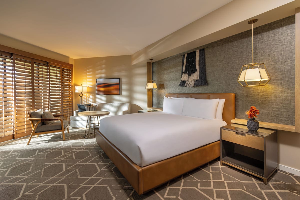 Ein Hotelzimmer mit einem großen Bett, einem Nachttisch mit Lampe, einem Sessel und einem kleinen Tisch.