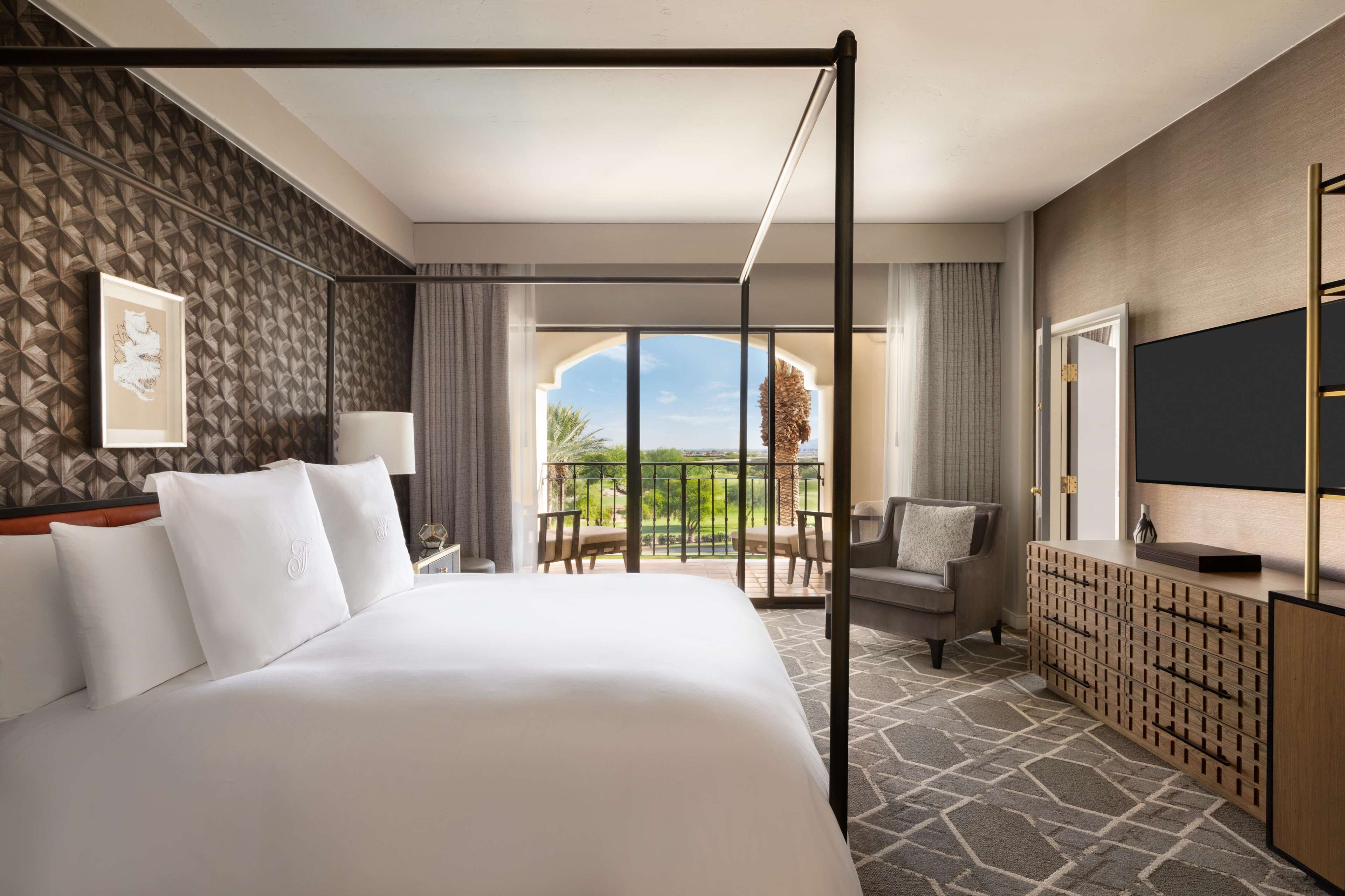 Une chambre d’hôtel avec un grand lit, un balcon avec vue, une télévision et un bureau avec une lampe.