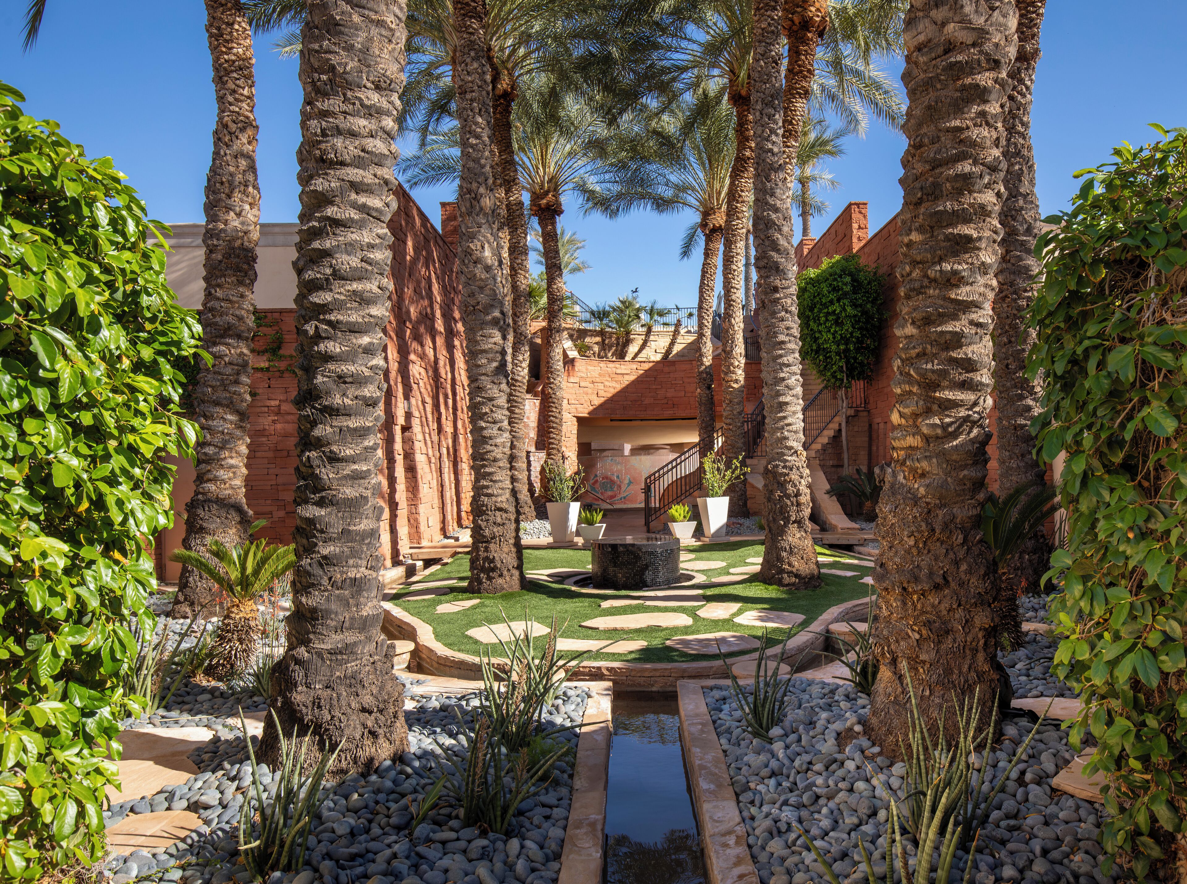 A courtyard with palm trees, a brick wall, and a small water feature.