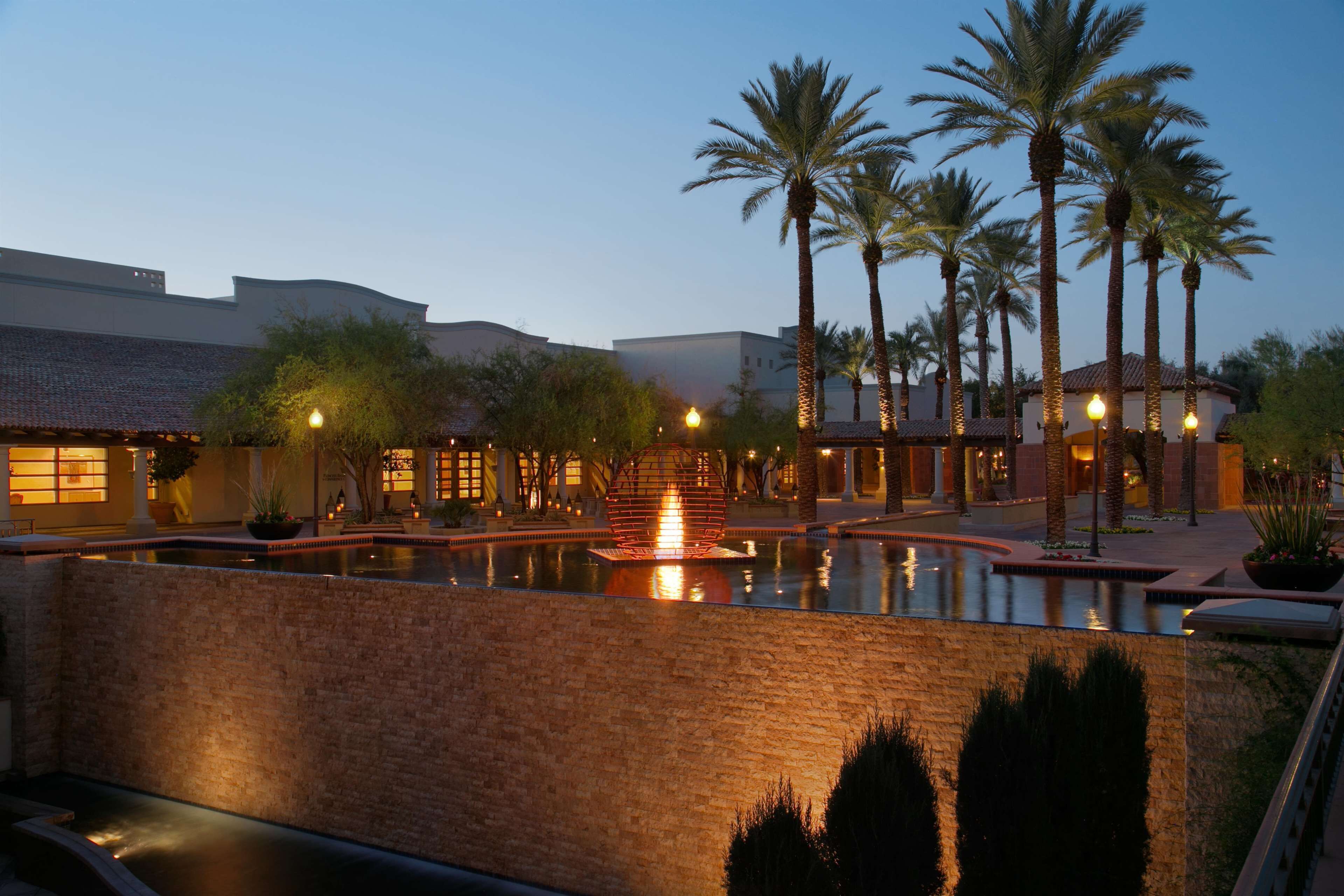 A hotel courtyard with a central fountain, palm trees, and brick walls.