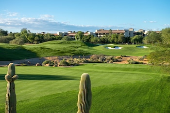 A hotel room with a bed, a sofa, a round table, a TV, and a window with curtains. at Fairmont Scottsdale Princess