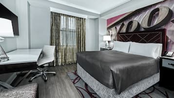 A hotel room with a large bed, a desk, a chair, a nightstand, and a large window with curtains.