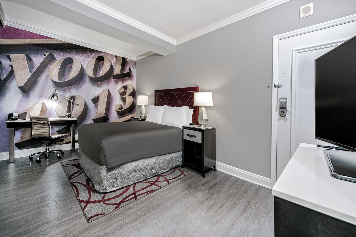 A modern hotel room with a large bed, a desk, a chair, a TV, and a wall with large numbers.