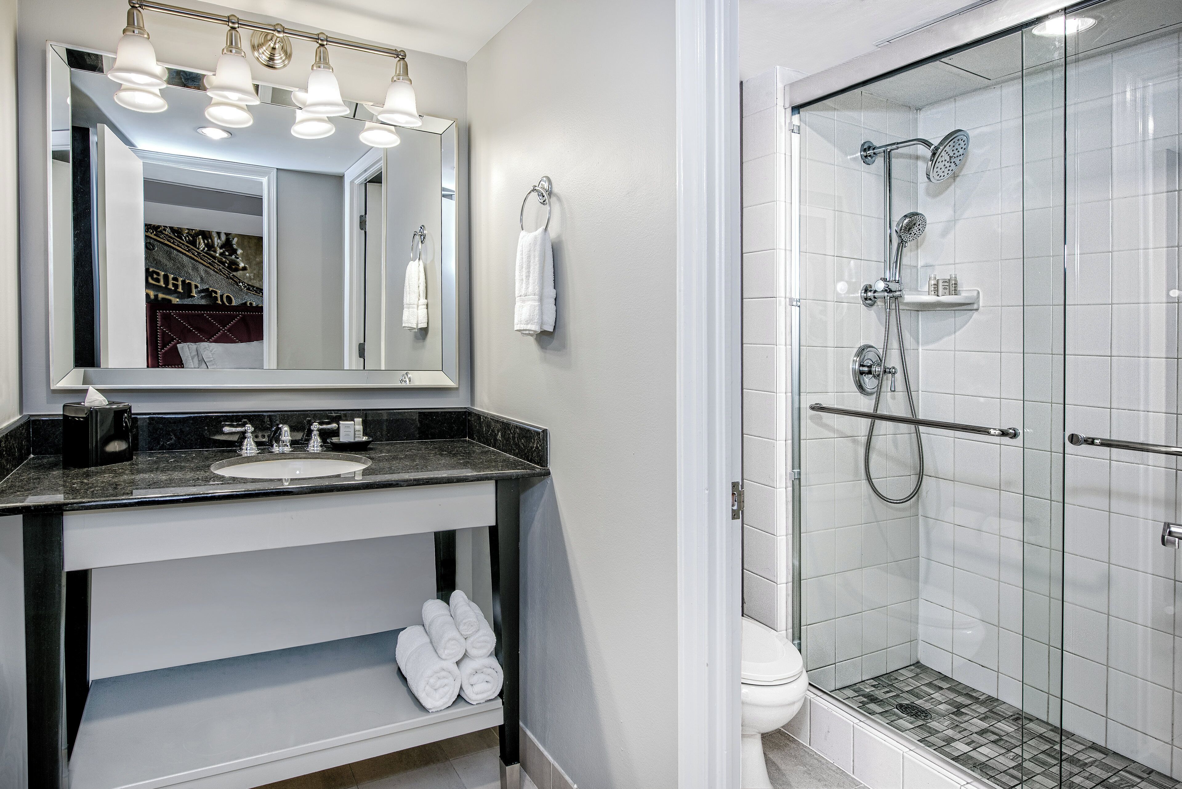 A bathroom with a mirror, sink, towel rack, and a shower area.