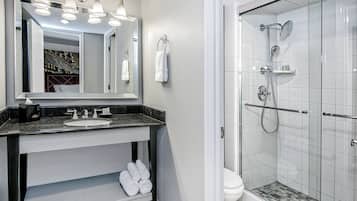 A bathroom with a sink, mirror, towel rack, and a glass-enclosed shower area.