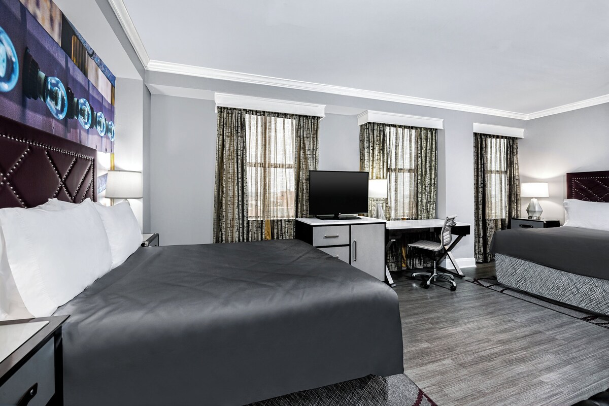 A hotel room with a bed, desk, chair, TV, and curtains.