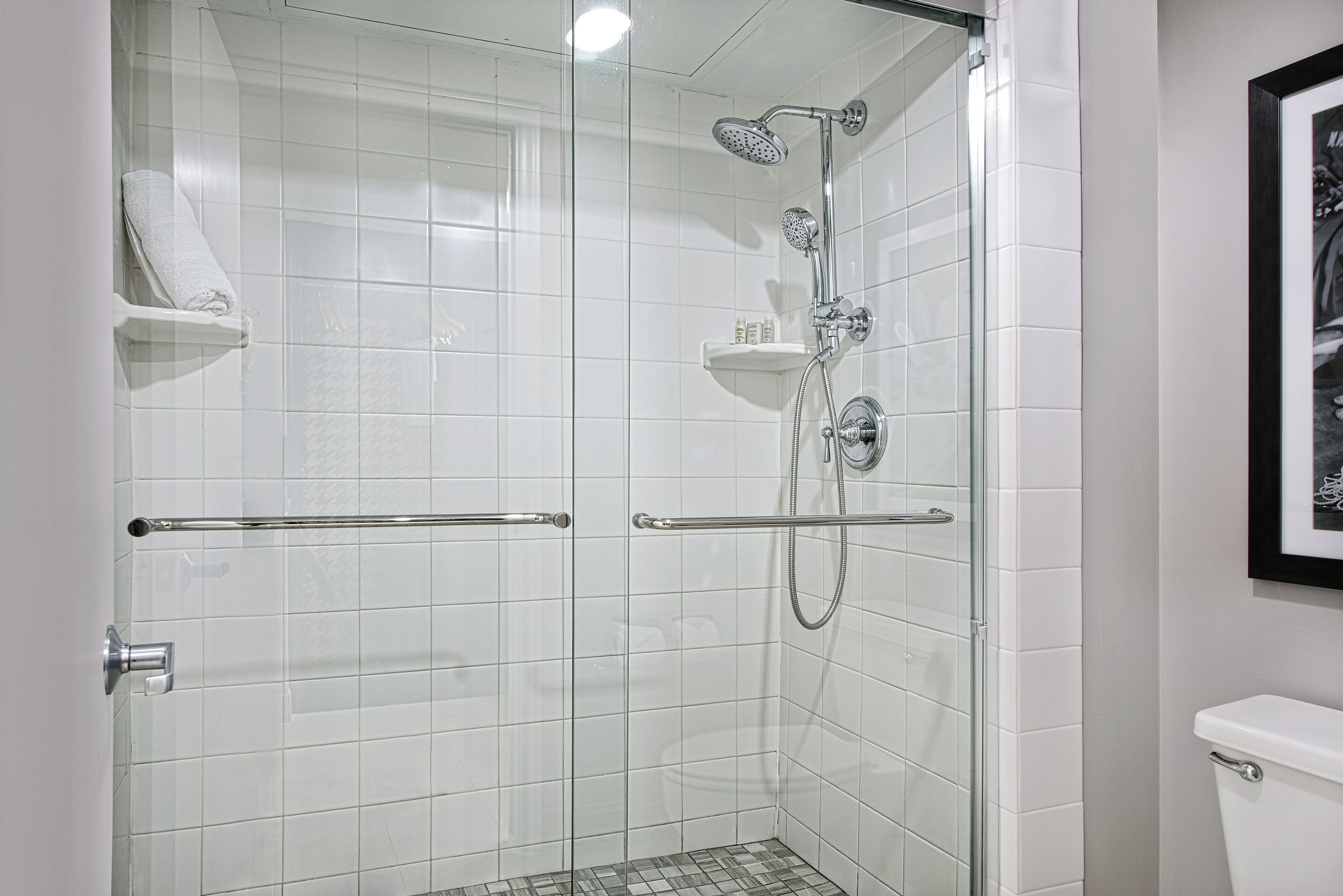 A glass-enclosed shower with a handheld showerhead and a wall-mounted faucet.