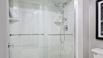 A glass-enclosed shower with a handheld showerhead and a wall-mounted faucet.