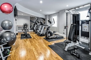 A gym with exercise equipment, wooden flooring, and a wall-mounted exercise ball. - Hotel Indigo Dallas Downtown by IHG (Dallas)