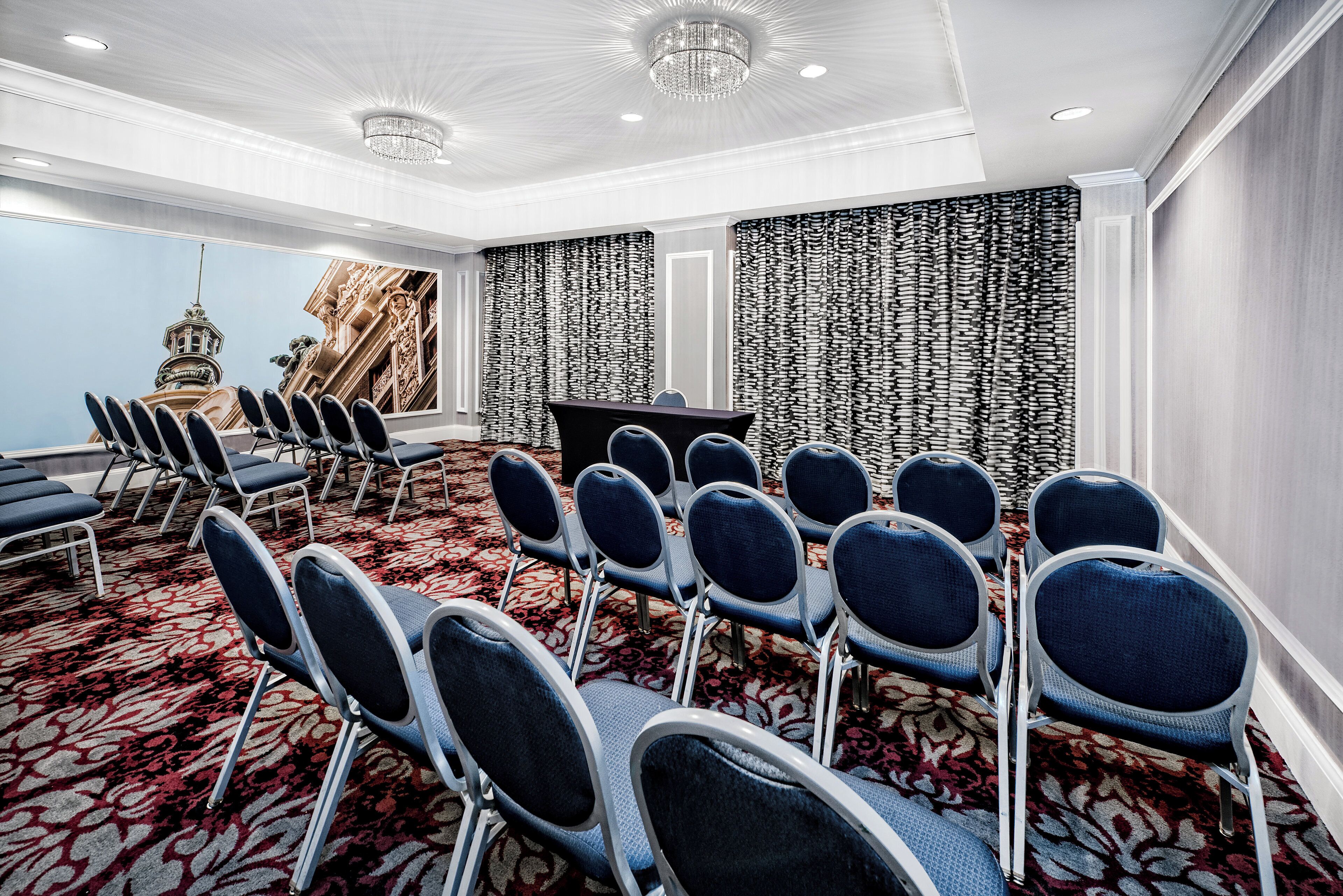 A conference room with rows of chairs, a large screen, and a patterned curtain backdrop.