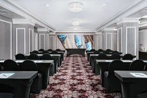 Un salón de conferencias con filas de mesas y sillas, una alfombra estampada y un ventanal con vista al cielo.