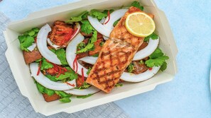 A box containing grilled salmon, sliced onions, and fresh herbs. - Hotel Indigo Dallas Downtown by IHG (Dallas)