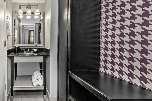 Un baño con espejo, lavamanos y toallero.