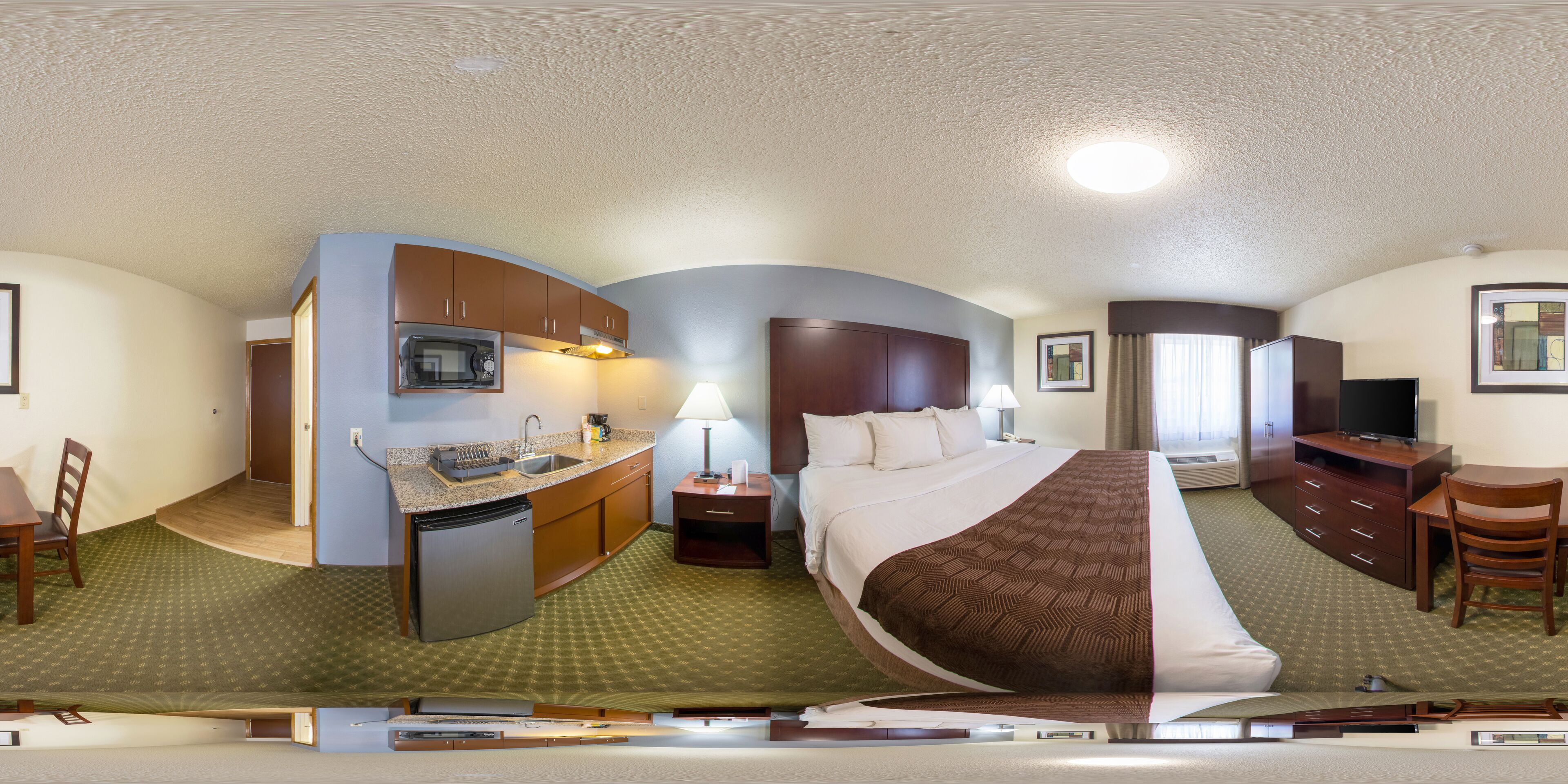 A hotel room with a kitchenette, a bed, a desk, and a TV.