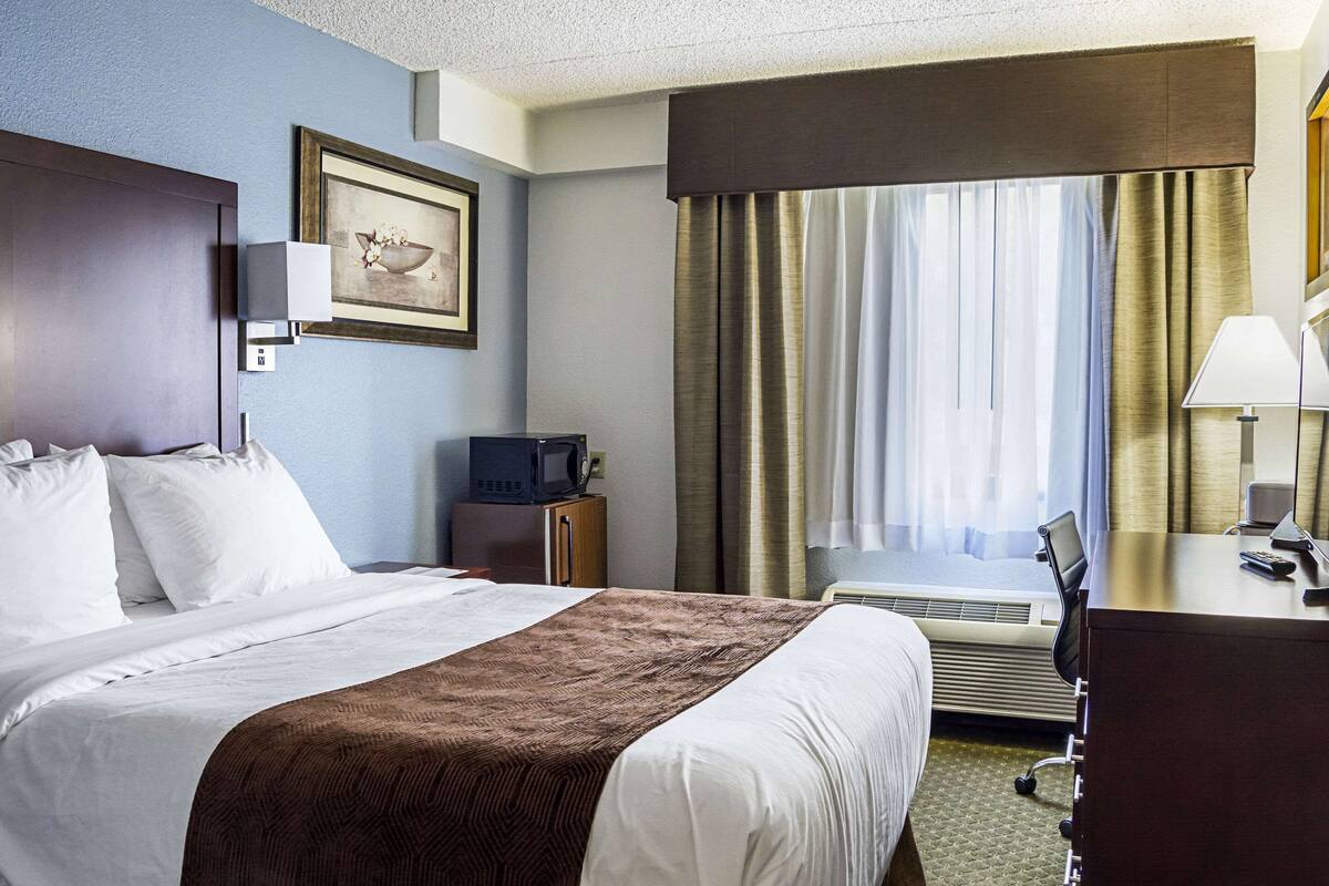 A hotel room with a bed, a desk, a chair, a television, and a window with curtains.