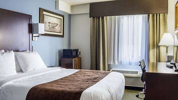 A hotel room with a bed, a desk, a chair, a television, and a window with curtains.