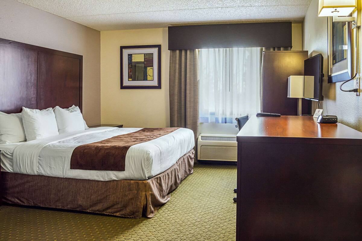 A hotel room with a large bed, a desk, a chair, a lamp, and a window with curtains.