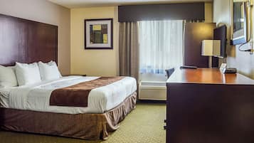 Ein Hotelzimmer mit einem großen Bett, einem Schreibtisch, einem Stuhl, einer Lampe und einem fenster mit Vorhängen.