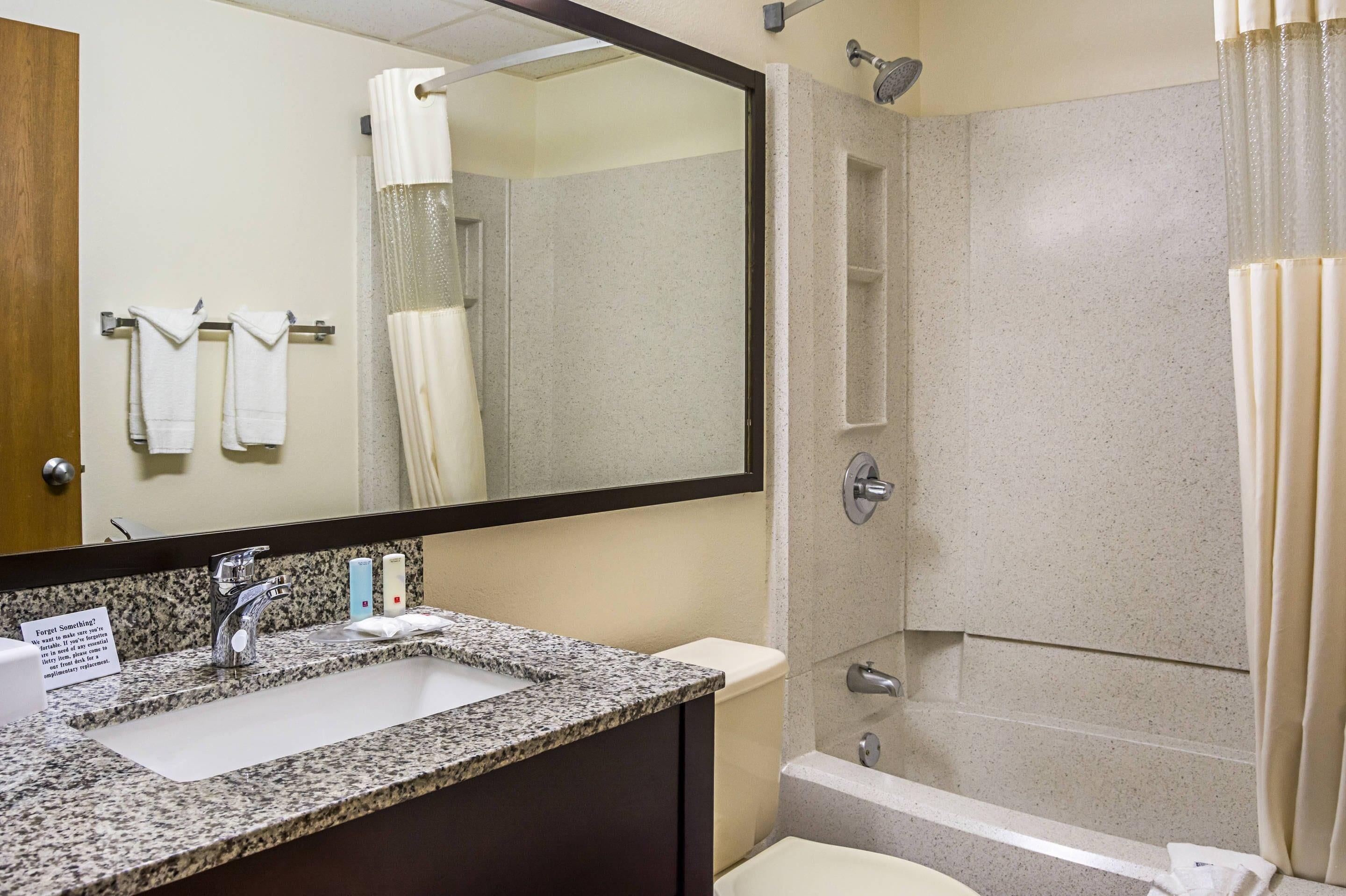 A bathroom with a granite countertop sink, a mirror, a shower with a glass door, and a towel rack with two towels.