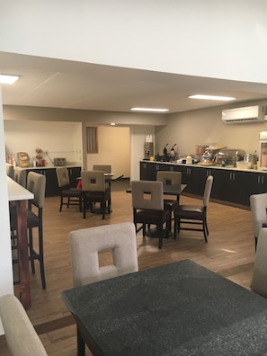 A modern kitchen with a dining area, featuring a granite countertop, dark cabinets, and a wooden floor.