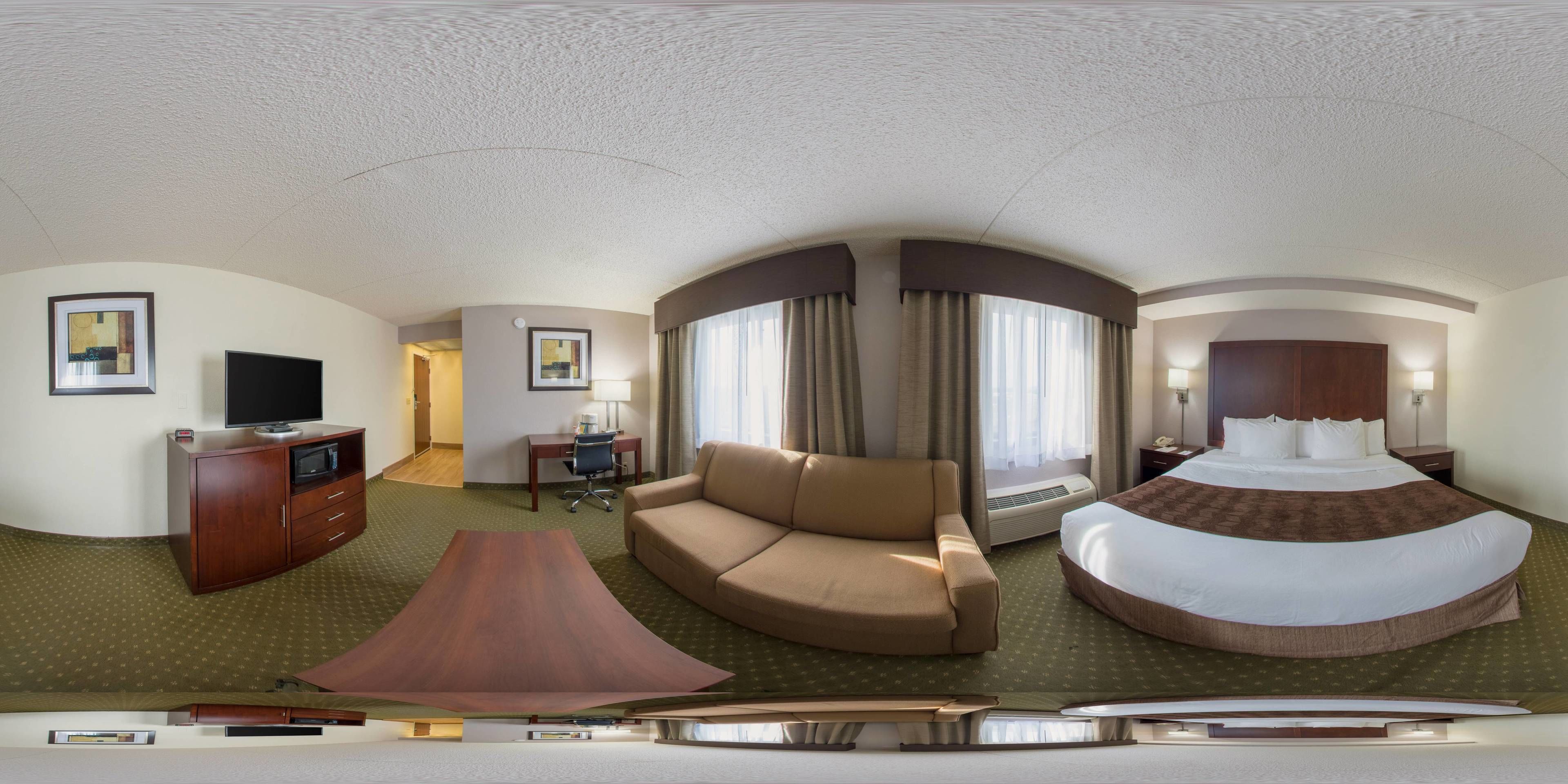 Habitación de hotel con una cama grande, un sofá, un escritorio con una silla, una televisión y un televisor de pantalla plana montado en la pared.