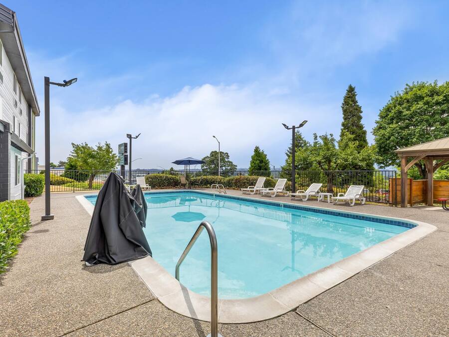 A swimming pool with lounge chairs, a covered area, and a building with a gray facade.