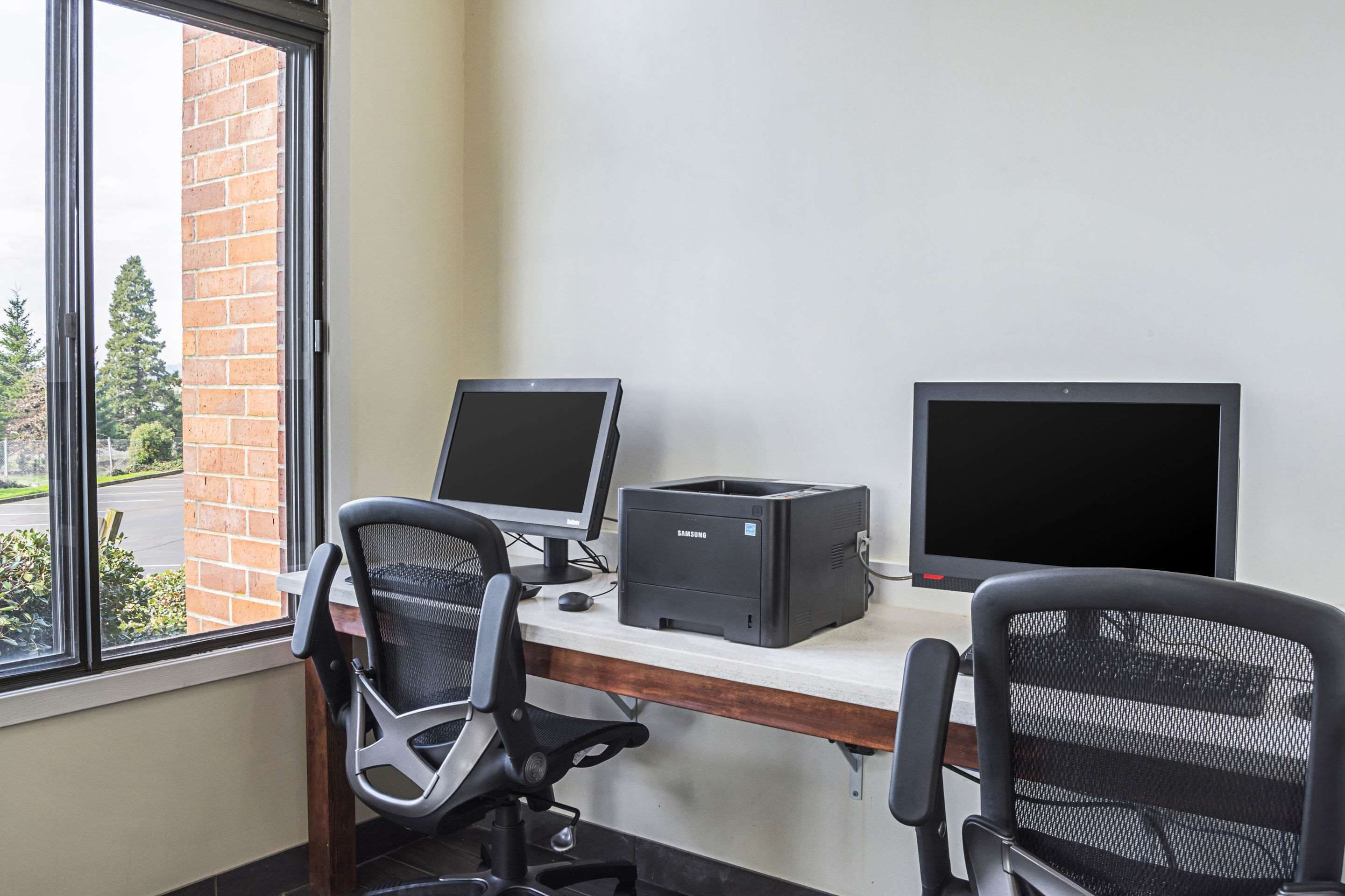 A workspace with two monitors, a printer, and two office chairs.