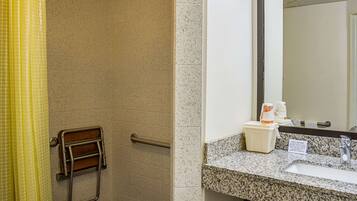 A bathroom with a handrail, a sink, a mirror, and a towel rack.