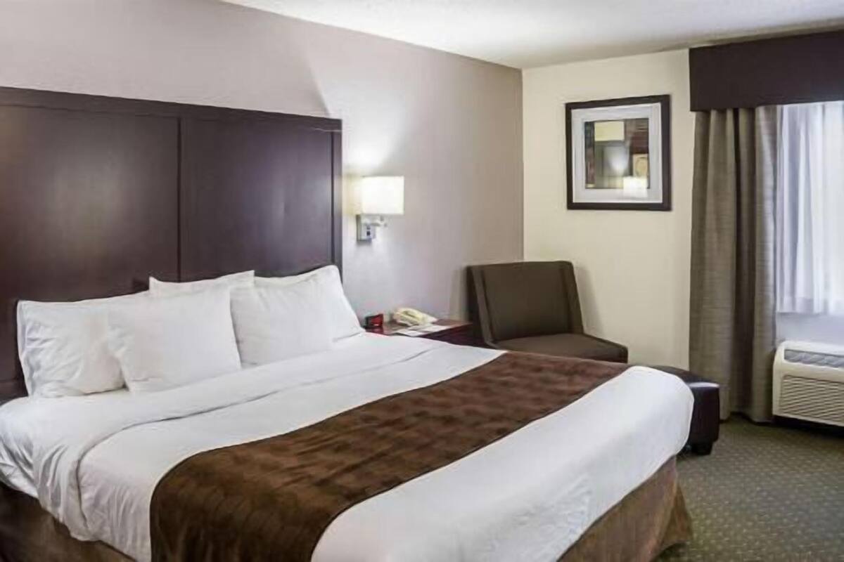 A hotel room with a large bed, a chair, a desk with a phone, and a window with curtains.