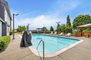 A swimming pool with lounge chairs, a covered area, and a building with a grey facade.