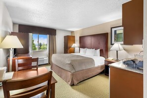 A hotel room with a bed, desk, chair, and a view of the outdoors. - Quality Inn & Suites Clackamas – Portland (Clackamas)