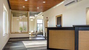 Ett välkomstområde med en receptionsdisk i trä, en modern takdesign och utsikt över en matplats med stolar och ett bord.