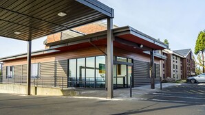 En modern byggnad med en inglasad entré, stora fönster och en parkeringsplats.