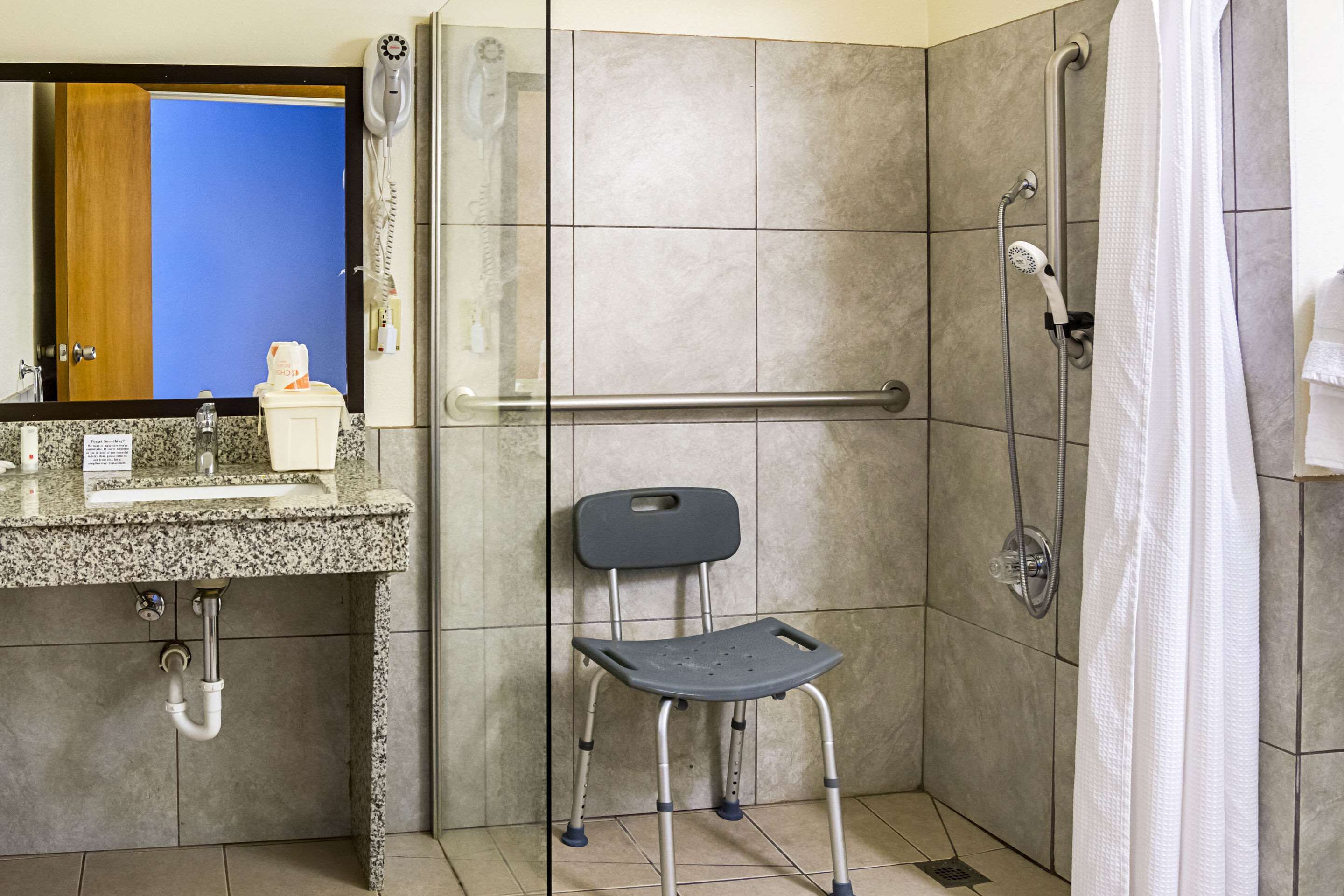Un baño con ducha, un secador de manos, un perchero y una silla.