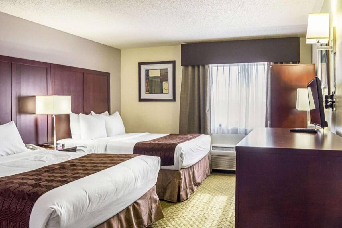 A hotel room with two beds, a desk, a lamp, a framed picture on the wall, and a window with curtains.
