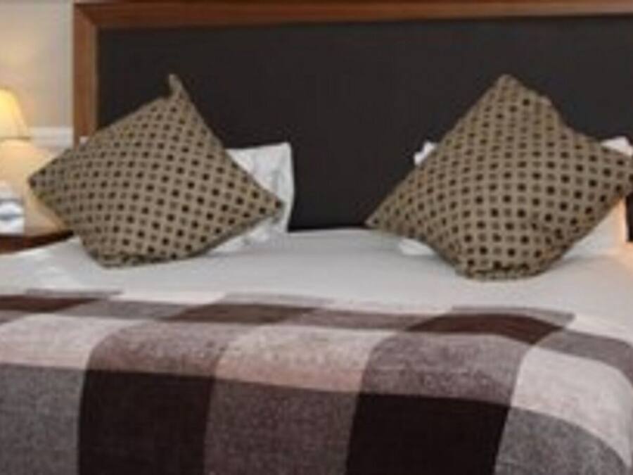 A hotel room with a large bed, two pillows, a checkered blanket, and two bedside lamps.