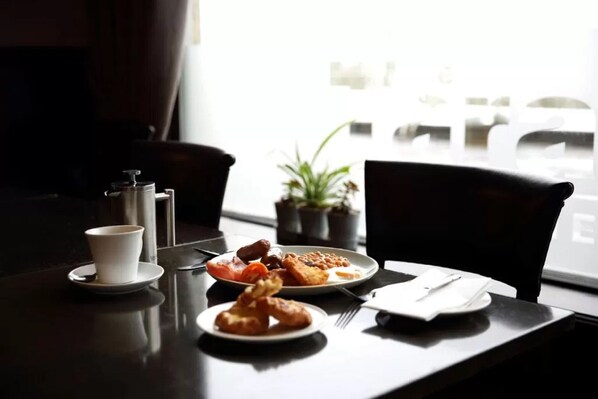 A dining table with a cup, plates of food, a plant, and a window view.