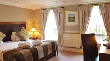 Habitación de hotel con cama, escritorio, silla, lámpara y un cuadro en la pared.