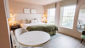 A hotel room with a bed, bedside tables, a round table, chairs, and large windows. - Hatton Court (Gloucester)